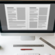Designer's desk with a monitor showing a right-aligned two-page layout, printed proofs, a ruler and a red proofing pen